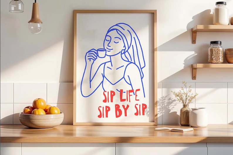 Pu&ograve; includere: Una stampa artistica da parete incorniciata con un disegno a linee blu di una persona con un asciugamano avvolto intorno alla testa, che tiene in mano una tazzina. Sotto l'illustrazione, il testo rosso recita SIP LIFE SIP BY SIP.