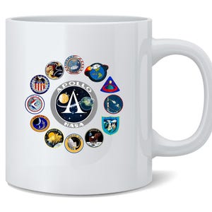 May include: White ceramic mug featuring a collection of Apollo space mission patches. The central design includes the Apollo NASA logo with a stylized 'A' and a depiction of the moon and Earth. The surrounding patches showcase various mission emblems.