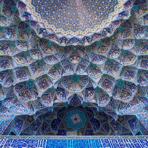 May include: Intricate ceiling design featuring a mosaic of blue, turquoise, and white tiles. The pattern is geometric, with floral and star-like motifs. The ceiling has a domed shape, creating a sense of depth and grandeur. The overall effect is ornate and visually stunning.