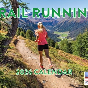 May include: A 2026 calendar with the words "TRAIL RUNNING" in green letters across the top. A woman in pink shirt and black shorts runs on a trail in the mountains. The calendar is made in the USA.