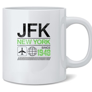 May include: White ceramic mug featuring the text "JFK NEW YORK SINCE 1948" in black and green. The design includes an airplane icon and a globe icon. The mug has a curved handle.