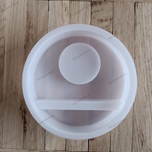 Könnte beinhalten: Eine weiße Silikonform mit kreisförmigem Design. Die Form hat einen großen äußeren Ring, einen kleineren inneren Kreis und ein horizontales Regal. Der Text "designed-4you" wiederholt sich an den Rändern.