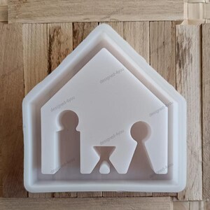 Könnte beinhalten: Eine weiße Silikonform in Form einer Krippenszene. Die Form hat einen Hausumriss mit Ausschnitten von Figuren und einem Tisch. Der Text "designed-4you" ist sichtbar.