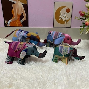 Op de afbeelding: Vier kleurrijke stoffen olifantenbeeldjes met patchwork-ontwerpen. Elke olifant heeft een ander kleurenschema, waaronder blauw, roze, groen en geel, met gedetailleerde patronen op hun oren en rug. De olifanten worden tentoongesteld op een witte, zachte ondergrond.