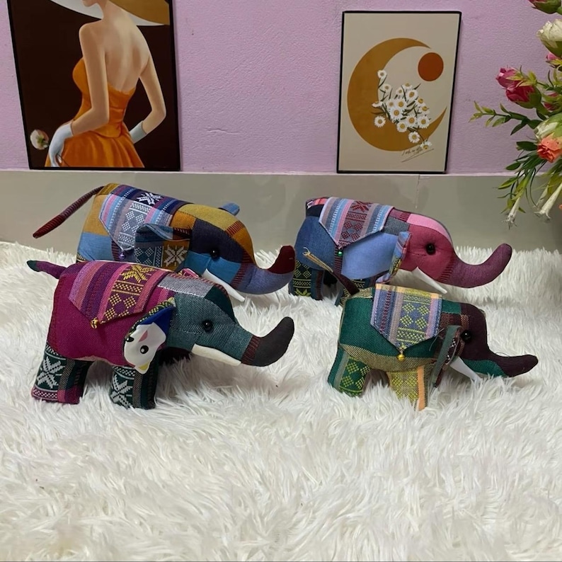 Op de afbeelding: Vier kleurrijke stoffen olifantenbeeldjes met patchwork-ontwerpen. Elke olifant heeft een ander kleurenschema, waaronder blauw, roze, groen en geel, met gedetailleerde patronen op hun oren en rug. De olifanten worden tentoongesteld op een witte, zachte ondergrond.