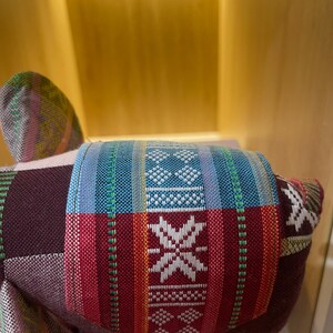 Op de afbeelding: Een kleurrijk, handgemaakt stoffen olifantenspeelgoed. De olifant heeft een patchwork-ontwerp met levendige rode, blauwe en witte patronen. Een kleine blauwe kraal hangt aan de onderkant. Het speelgoed is gemaakt van geweven stof.