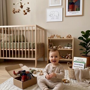Op de afbeelding: Een babykamer met een houten ledikant, planken en ingelijste kunst. Een baby zit op een kleed omringd door speelgoed. Een mobiel met vilten dieren hangt boven de wieg. Een open kartonnen doos bevat een stoffen olifant.