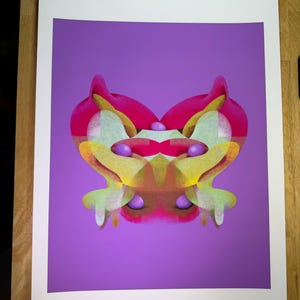 May include: Abstract art print featuring a symmetrical design with a purple background. The artwork showcases a vibrant mix of colors, including pink, yellow, and green, creating a visually striking composition. The print is on white paper.