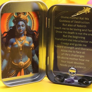 May include: A small, open metal tin featuring an illustration of the Hindu goddess Kali Ma. The tin also contains a skull, crystals, and text that reads "Divine mother Kali Ma Goddess of Destruction..." The background is yellow and pink.