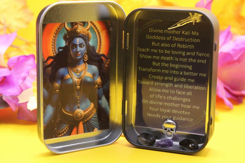 May include: A small, open metal tin featuring an illustration of the Hindu goddess Kali Ma. The tin also contains a skull, crystals, and text that reads "Divine mother Kali Ma Goddess of Destruction..." The background is yellow and pink.