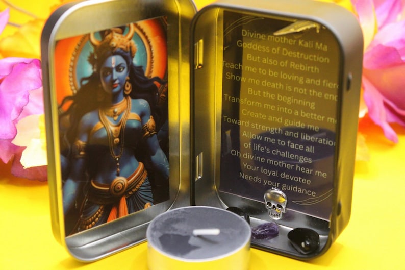 May include: A small, open metal tin featuring an image of a blue-skinned deity with gold accents. The tin also contains a small candle, a skull charm, and gemstones. Text on the inside panel reads "Divine mother Kali Ma Goddess of Destruction..."