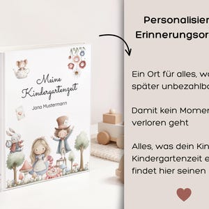 May include: A white personalized memory binder with the title "Meine Kindergartenzeit" and the name "Jana Mustermann" in script. The cover features whimsical illustrations of storybook characters and flowers. The binder's spine also has the title.