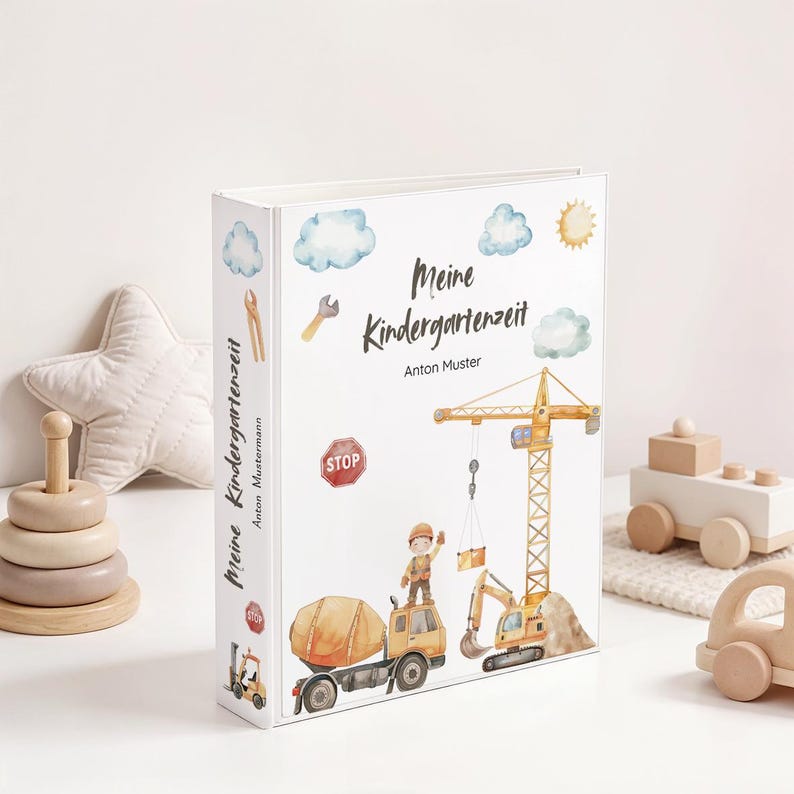May include: A white binder with the text "Meine Kindergartenzeit" and the name "Anton Muster" is decorated with construction-themed illustrations. The cover features a crane, excavator, cement truck, and a construction worker. Additional illustrations include clouds, a sun, and tools.