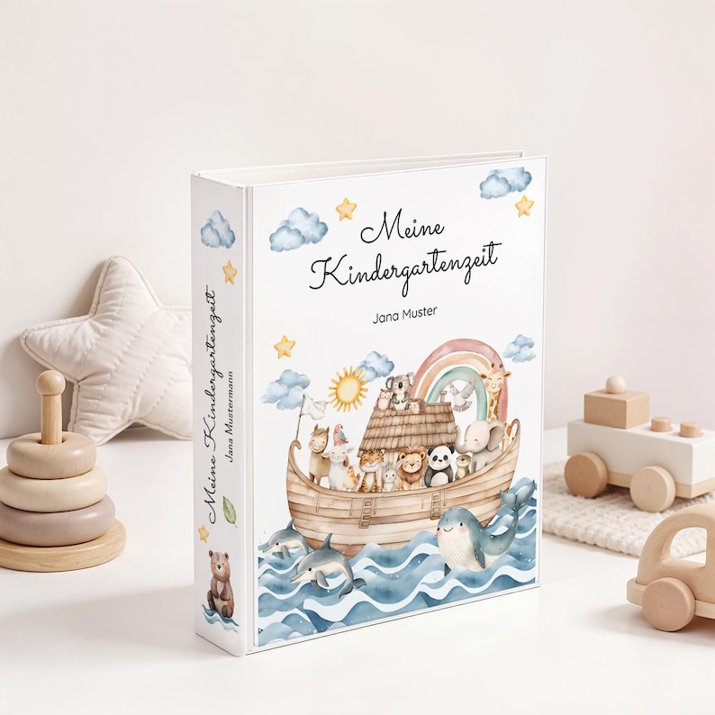 May include: A white binder with the German text "Meine Kindergartenzeit" and an illustration of an ark filled with animals, a rainbow, and a sun. The binder has a whimsical, watercolor style and is decorated with stars and clouds.