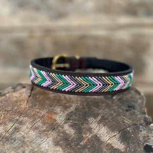 Könnte beinhalten: Ein braunes Leder-Halsband für Hunde mit einem Perlen-Zickzackmuster in Rosa, Grün, Gold und Schwarz. Das Halsband hat eine goldfarbene Schnalle und eine schwarze Innenseite.