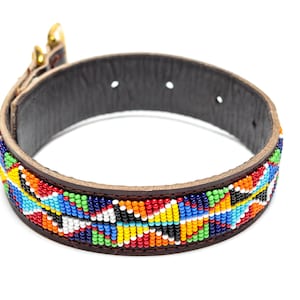 Op de afbeelding: Een hondenhalsband met een donkerbruine leren basis en een levendig kralenontwerp. De kralen zijn gerangschikt in een geometrisch patroon met kleuren als rood, blauw, geel, groen en wit. De halsband heeft een goudkleurige metalen gesp.