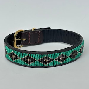 Peut inclure: Un collier de chien en cuir noir avec un motif de perles turquoise, noires et argentées. Le collier est doté d'une boucle dorée et d'un accent en cuir marron foncé près de la boucle.