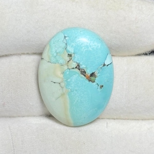 Pode incluir: Gema oval de turquesa, azul claro com veios castanhos escuros e pretos. A pedra polida tem um aspeto natural. A gema está sobre um fundo branco. Mede aproximadamente 2,5 cm de comprimento.