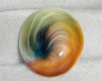 May include: A polished, oval-shaped gemstone with a swirling pattern of colors. The gem features shades of yellow, orange, brown, green, and blue. The surface is glossy and reflects light, showcasing the natural patterns within the stone.