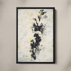 Pode incluir: Uma peça de arte de parede retangular com uma composição abstrata com um grupo vertical central de formas pretas semelhantes a tinta, acentuadas por salpicos brancos e pequenas marcas amarelas, num fundo esbranquiçado texturizado numa moldura flutuante preta.