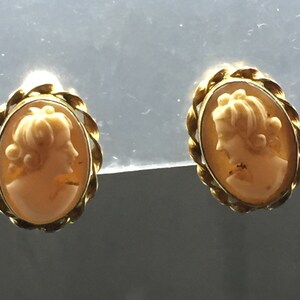 Könnte beinhalten: Ein Paar goldfarbene Kameenohrringe mit einem Seilrand. Jeder Ohrring zeigt ein Kamee mit dem Profil einer Frau.