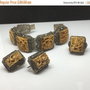 Puede incluir: Un conjunto de joyas vintage que incluye un brazalete de plata, un anillo y unos pendientes. El brazalete y los pendientes están decorados con cuadrados tallados de color marfil con diseños intrincados. El anillo es cuadrado con un diseño similar.