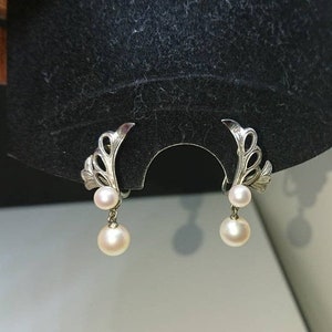 May include: A pair of silver earrings with a delicate floral design and two white pearls dangling from each earring.