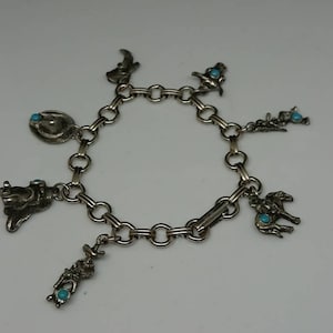 May include: A silver charm bracelet with turquoise stones and western-themed charms, including a cowboy hat, a cowboy riding a horse, and a boot.