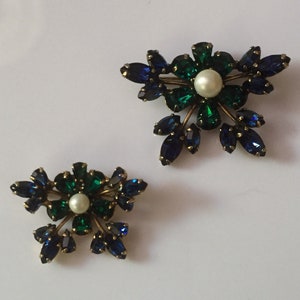May include: A pair of vintage brooches featuring a floral design with blue and green rhinestones and a pearl center.