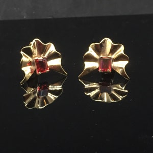 Op de afbeelding: Een paar gouden oorbellen met rode edelsteen accenten. De oorbellen zijn gevormd als een waaier met een gegolfde rand.