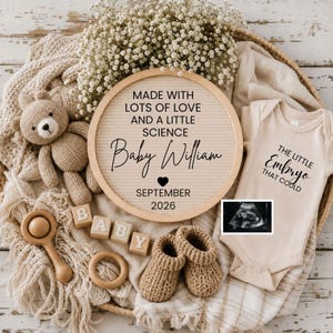 May include: A beige-toned baby announcement with a felt letter board that reads "Made with lots of love and a little science Baby William September 2026." Includes a teddy bear, baby booties, a onesie with text, wooden blocks spelling "BABY", and a sonogram.