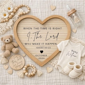 Puede incluir: Un letrero de madera en forma de corazón con el texto "WHEN THE TIME IS RIGHT, 9. The Lord WILL MAKE IT HAPPEN. ISAIAH 60:22 OCTOBER 202X." Un body y patucos blancos para bebé están junto al letrero. Un osito de peluche y un biberón también están en la imagen.
