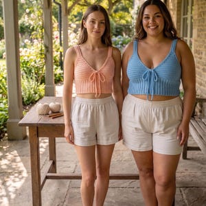 May include: Two crochet crop tops with V-necklines and front tie closures. One top is peach-coloured and the other is light blue. Both tops feature wide shoulder straps and a ribbed hem design, paired with plain off-white shorts.