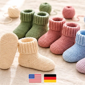 May include: A collection of handmade crochet baby booties in various pastel colors including cream, sage green, dusty rose, light blue, and lavender. Each pair features a ribbed cuff and a textured sole. A wooden crochet hook and yarn balls are present.