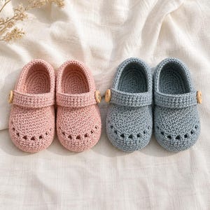 May include: Two pairs of handmade crochet baby shoes, one pair in soft pink and one pair in dusty blue. Each shoe features a rounded toe with small ventilation holes, a strap across the top secured by a small wooden button, and a textured yarn finish.