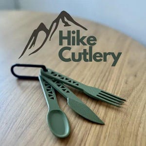 May include: Green Hike Cutlery set with a spoon, knife, and fork, connected by a black carabiner. The utensils have a geometric design and are displayed on a wooden surface. The Hike Cutlery logo is visible.
