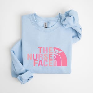 A light blue t-shirt with the text "THE NURSE FACE" printed on it in pink and white colors.
