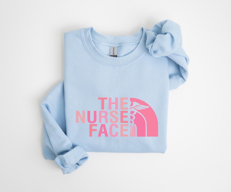 A light blue t-shirt with the text "THE NURSE FACE" printed on it in pink and white colors.