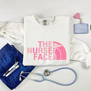 a white t-shirt with a pink logo, a stethoscope, a watch, a bracelet, and some other medical or nursing-related items.