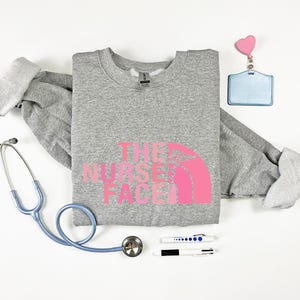 a gray sweatshirt with a pink logo, a stethoscope, a name tag, a pen, and a heart-shaped charm.