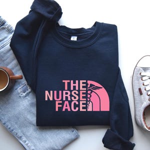 A casual outfit consisting of a navy blue sweatshirt with a pink logo, a pair of jeans, a pair of sneakers, and a cup of coffee.
