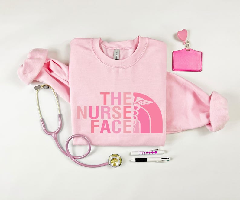 a pink t-shirt with the text "THE NURSE FACE" printed on it, along with a stethoscope, a badge, and some pens.