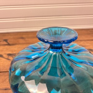 May include: A clear, turquoise glass bowl with a pedestal base. The bowl features a fluted design with a swirl pattern. The base is a solid, round shape. The bowl is likely for serving or display.