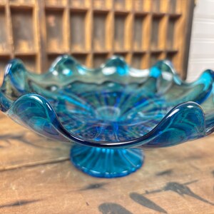 May include: A striking blue glass bowl with a scalloped edge and a pedestal base. The bowl features a swirling, textured design in shades of teal and blue. This decorative piece is suitable for serving or display.