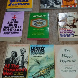 K&ouml;nnte beinhalten: Eine Sammlung von Vintage-B&uuml;chern mit farbenfrohen Einb&auml;nden. Zu den Titeln geh&ouml;ren "Without Feathers" von Woody Allen, "Zen and the Art of Motorcycle Maintenance" und "All the President's Men". Die B&uuml;cher liegen auf einer Holzoberfl&auml;che.