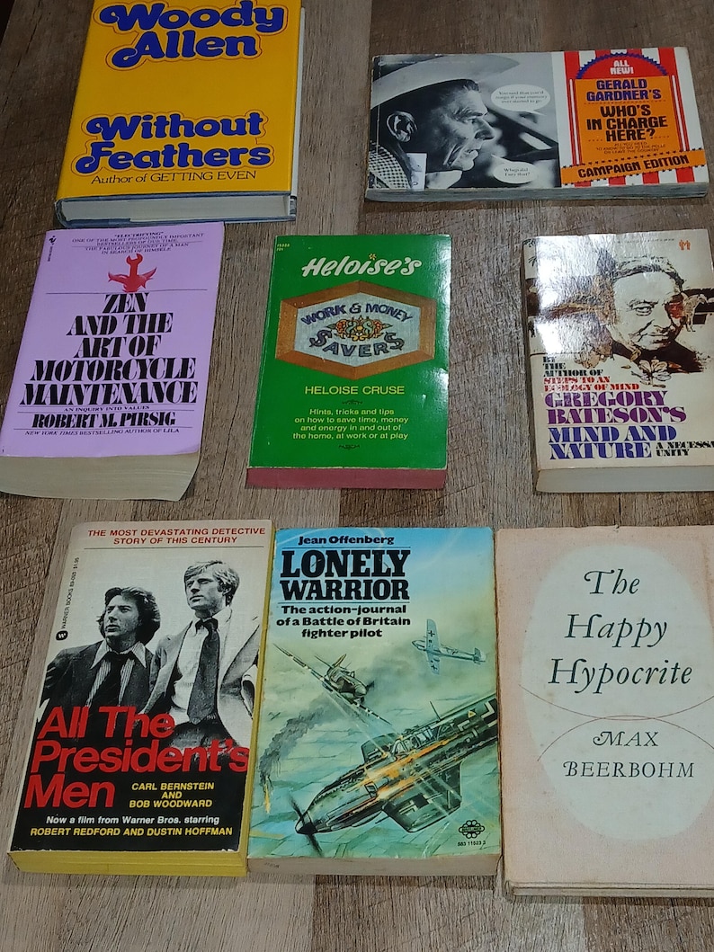 K&ouml;nnte beinhalten: Eine Sammlung von Vintage-B&uuml;chern mit farbenfrohen Einb&auml;nden. Zu den Titeln geh&ouml;ren "Without Feathers" von Woody Allen, "Zen and the Art of Motorcycle Maintenance" und "All the President's Men". Die B&uuml;cher liegen auf einer Holzoberfl&auml;che.
