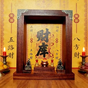 Può includere: Un altare in legno con una cornice marrone scuro e angoli in ottone. L'altare presenta un pannello centrale con caratteri cinesi e una piccola piattaforma che ospita un incensiere, due piccole statue e due candele rosse. Lo sfondo è giallo con testo cinese.