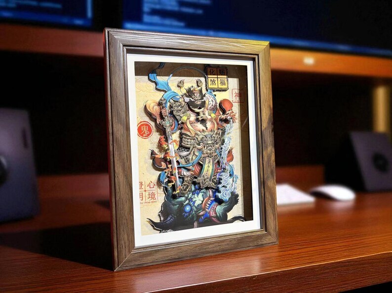 May include: Framed 3D paper art depicting a detailed, colorful Asian deity with a sword, set against a cream background. The artwork is in a wooden frame, with Chinese characters visible. The overall theme is cultural art.