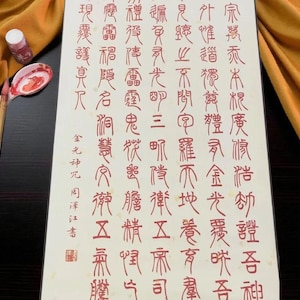 May include: A calligraphy set featuring a sheet of paper with red Chinese characters, a small ink bottle, and a spoon-like tool. The paper has vertical text. The spoon has a red floral design.