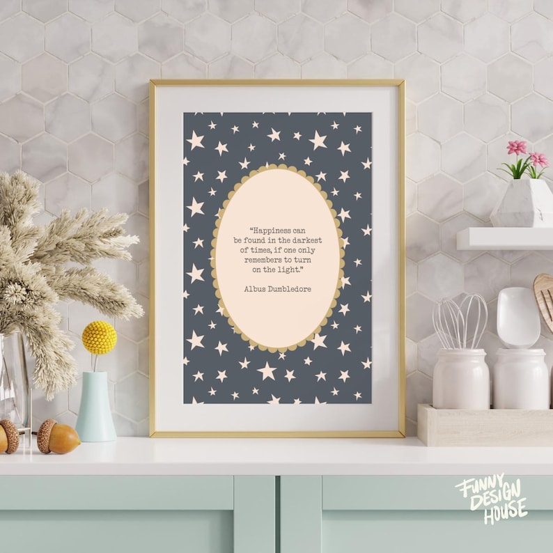 May include: A framed print with a gold border features a quote by Albus Dumbledore on a starry background. The quote reads, "Happiness can be found in the darkest of times, if one only remembers to turn on the light."